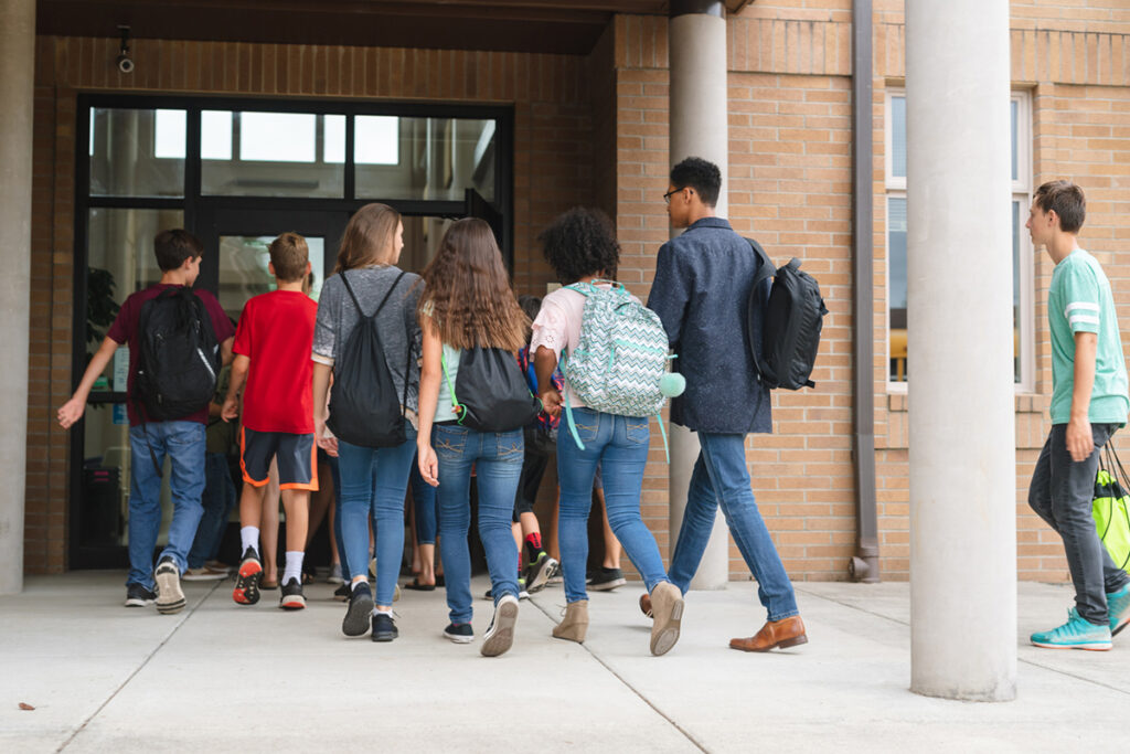 Students walk in the front entrance to school early in the morning. The shot is from behind.