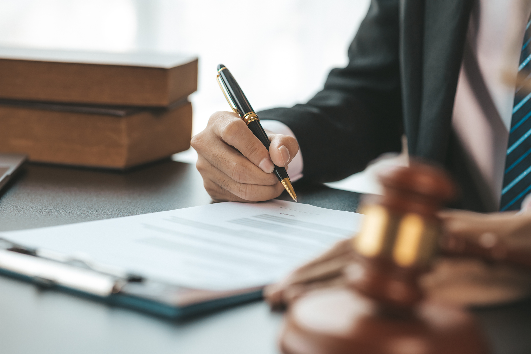 A lawyer sits in his office, on a table with a small gavel and writing on a document
